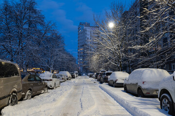 Street and cars covered in a thick layer of snow on a winter evening