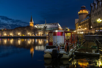 Tourist boat on the river, reflected at dusk, with the Fishing Village promenade and Kaliningrad Cathedral in the background