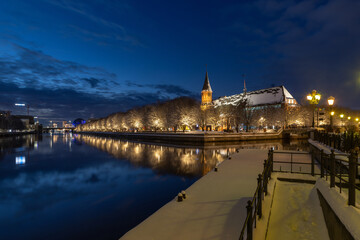 The snow-covered embankment of the Fishing Village with Kaliningrad Cathedral in the background, reflected in the river on a winter evening