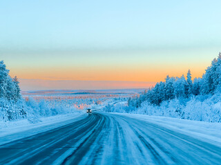 Empty Asphalt Highway Stretching Through a Frozen Winter Forest with Golden Sunset Light on Tree Tops