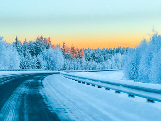 Empty Asphalt Highway Stretching Through a Frozen Winter Forest with Golden Sunset Light on Tree Tops