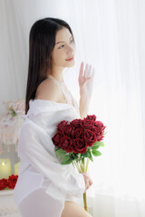 Asian woman holding rose bouquet looking out window with hope and waiting