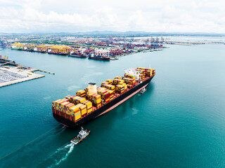 Aerial view of large cargo container ship being towed by tugboats to enter industrial port terminal for international business logistics and trade transportation.