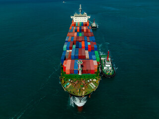 Aerial top view of cargo container ship with tugboat assistance maneuvering in harbor