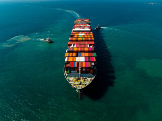 Aerial top view of cargo ship maneuvering with tugboats for logistics management business
