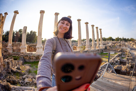 A tourist takes a selfie against the backdrop of columns and an archaeological site. The photo is taken from a low angle. creates content for social media. Israel, Beit She'an.