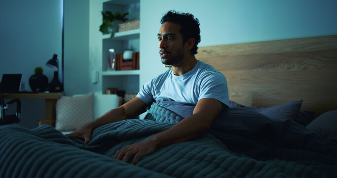 Insomnia, scared and man in bedroom at night for burnout, exhausted and fatigue for mental health. Tired, dark and person with fear, awake and afraid for sleepless, bad dream and nightmare in home