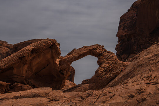 View of a natural archway of red sandstone against a muted sky, sculpted by time and the elements in the Valley of Fire State Park, Overton, Nevada, United States.