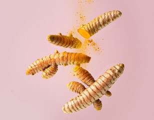 Naklejka premium Floating turmeric roots with vibrant golden powder on pastel pink background, creative minimal food styling for healthy cooking and natural wellness concepts