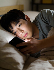 Young asian man using mobile phone on the bed