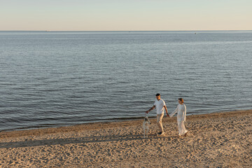 Happy young couple with a dog on the beach. Pregnant woman with a man and a dog on a walk, family