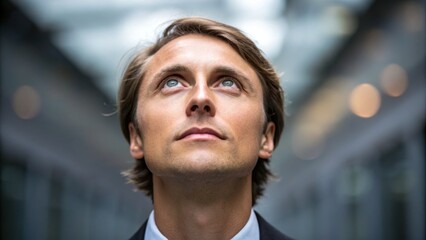 Man gazing upwards with a thoughtful expression in a modern indoor setting.
