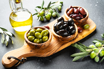 Olives in wooden bowl at black background.
