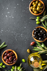 Olives in wooden bowls and Olive oil in the bottle at black table.