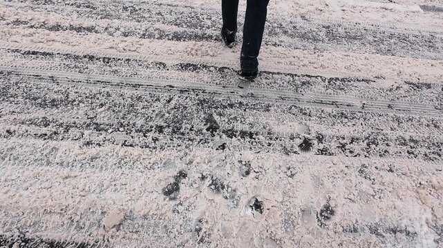 Pedestrian crossing a snow-covered road. Dangerous winter weather and slippery conditions. A pedestrian crossing covered in snow after a snowstorm.