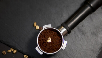 Espresso portafilter filled with ground coffee featuring a single golden coffee bean, surrounded by...