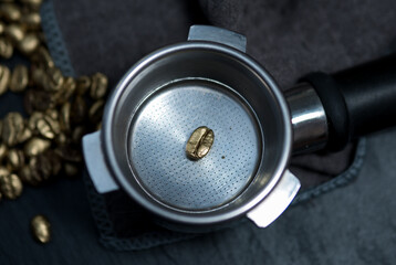 Single golden coffee bean placed in an espresso portafilter, surrounded by gold-colored...