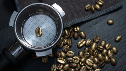 Single golden coffee bean placed in an espresso portafilter, surrounded by gold-colored...