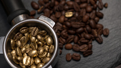 Fototapeta premium Top view of golden coffee beans filled in an espresso portafilter, surrounded by regular roasted beans on a dark background.