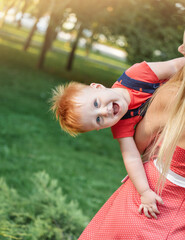 Happy laughing baby boy. Mom and son are playing together in the park in the summer. Mother is holding kid in her arms.