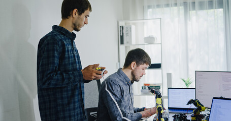 Team adult male engineer collaborate on robotic hand project using AI code solutions machine learning at tech workspace. Artificial intelligence interface, collaboration support prototype development.