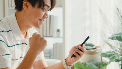 Close up youth Asia male with casual cloth sit on sofa looking at smartphone feel excited with...
