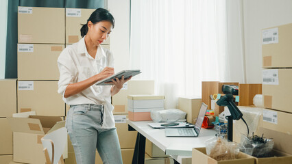 Youth attractive Asia female entrepreneur small business use digital tablet check parcel counting cardboard box in confirm check stock inventory product ready for shipment at small online retail shop.