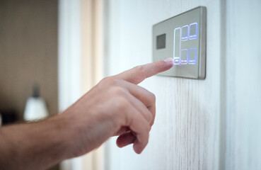 Hand pressing modern smart home control panel with illuminated buttons, showcasing advanced technology and user interaction in a contemporary living space