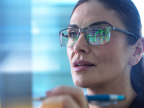 Financial analyst analyzing market data with charts reflected in glasses