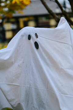 Child in ghost costume fooling around outdoors during Halloween in autumn