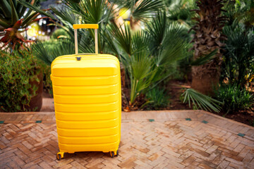 Bright yellow suitcase stands on patterned stone pathway surrounded by lush green tropical plants, symbolizing travel, adventure, and exploration in a vibrant outdoor setting