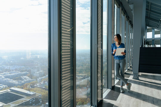 Businesswoman holding tablet PC and looking through window in office