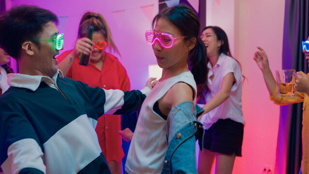 Diverse group multiethnic young adult Asia friend wear futuristic neon glowing glasses dance and drink alcohol beer fun hangout party in living room night indoor home. Disco lights illuminating house.
