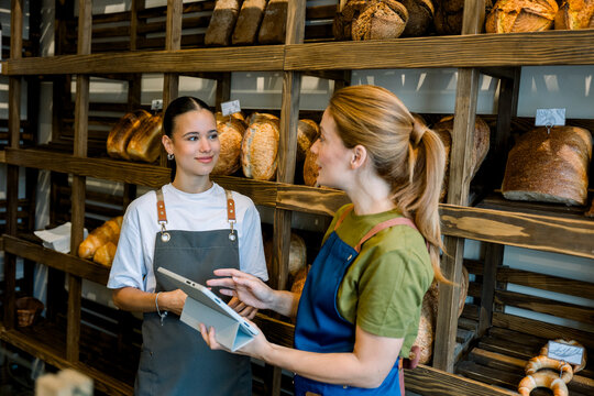 Experienced baker explaining work to trainee using tablet in bakery