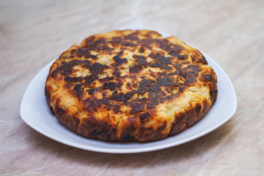 Homemade round baked casserole or pie with golden brown crust on white plate. Rustic cottage cheese or meat dish.