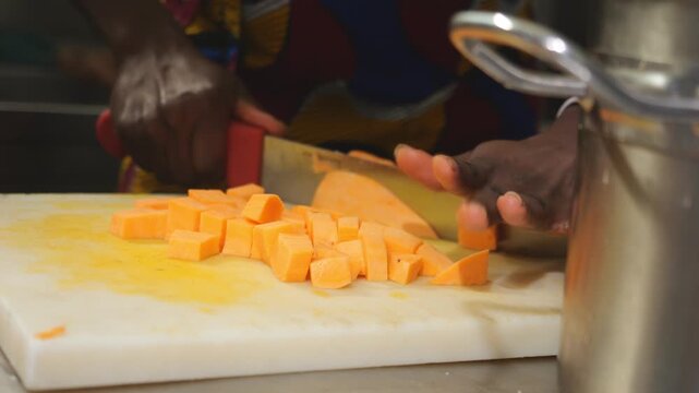 African female chef cutting and slicing peeled yams within a professional kitchen environment, slow motion shot