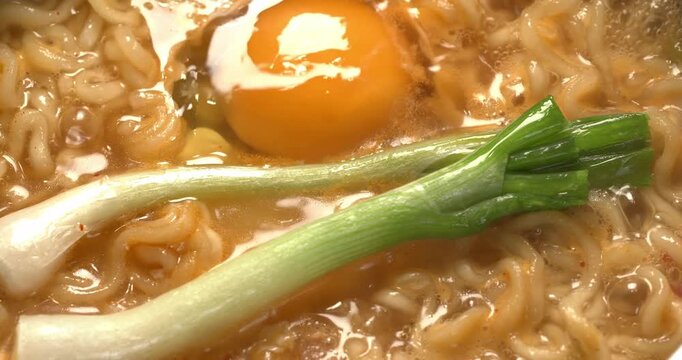Green onions are added to boiling water with instant noodles and egg. The process of making Korean spicy  ramyong soup.