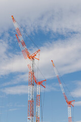 3基の赤白に塗装された建設用クレーンと青空