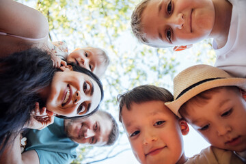 Group of children and adults smiling together, captured from a low angle, surrounded by greenery, showcasing joy and connection in a playful outdoor setting
