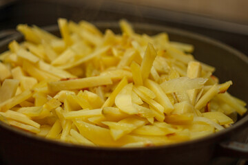 Fried golden potatoes cooking in a pan close up. Delicious homemade roasted potato strips dish...