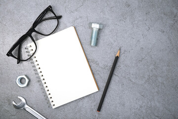 Notebook with glasses and wrench on stone texture background. Business desk office. Top view