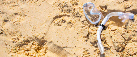 Snorkel mask and tube lying on sandy beach. Summer vacation scene representing sea exploration and travel lifestyle.