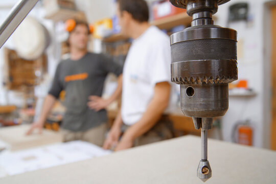 Drill and two carpenters in conversation at woodworking workshop