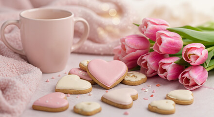 Pink cup with heart-shaped cookies and tulips on soft background  