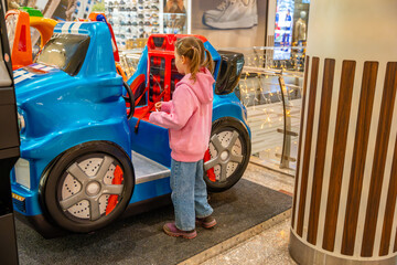 Little girl riding coin operated toy car attraction in shopping mall kids area. Childhood...