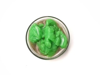 Indonesian green rice pudding with palm sugar syrup (Bubur sumsum pandan) served in a glass bowl isolated on white background. popular Indonesian street food and takjil for Iftar. Top view 