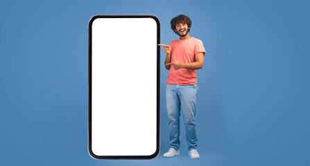 A person stands next to a large blank screen while smiling and pointing. The setting features a...