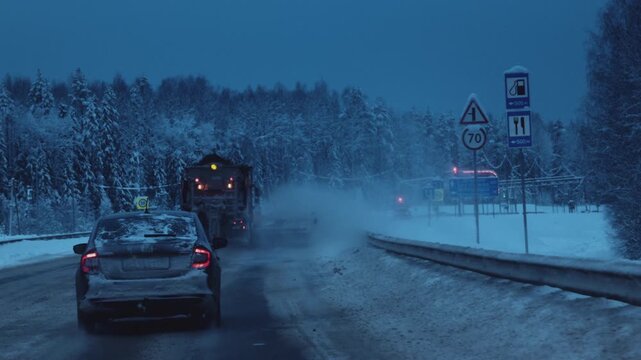 Clearing snow from the road in winter. Large industrial vehicle removes snow from the highway, sprinkles sand or chemicals. Polar night and snow storm, blizzard in arctic.