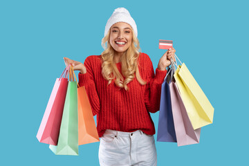 Winter Sale. Portrait of excited young lady in white hat holding credit card and colorful shopper...