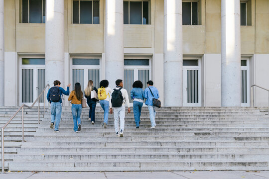 Group of diverse college students with backpacks walking up campus stairs toward an education building